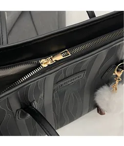 Close-up of golden metal zipper and plush charm on black patterned leather tote bag