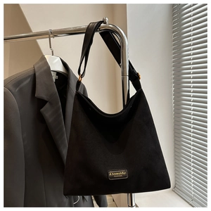 Detail of minimalist black faux suede shoulder bag with debossed fashion logo patch