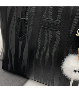 Detail of black tote bag with wave texture, brand logo and white fuzzy monster charm
