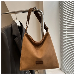Detail of a brown suede bucket bag with adjustable strap and embossed fashion label tag