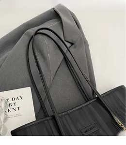 Detail of black tote bag with wave texture, leather strap and brand plaque on grey suit