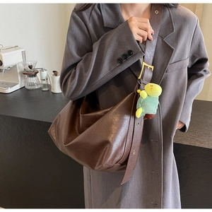 Detail of dark brown glossy leather crescent tote with adjustable strap and turtle charm