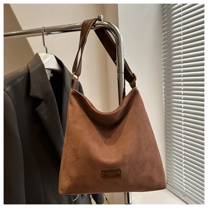 Close-up of brown suede bucket bag with wide shoulder strap and leather brand label