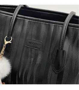 Detail of black tote bag featuring textured ripple patterns and white plush ball charm
