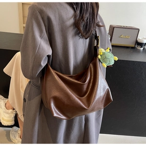Detail of deep brown glossy leather hobo tote bag featuring a green turtle plush charm
