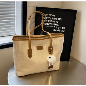 Detail of cream textured tote bag with brown leather trim and cute plush eye charm pendant