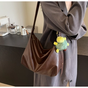 Detail of dark brown faux leather tote with vintage texture and green turtle pendant
