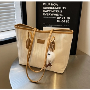 Detail of off-white tote bag with wave texture, brown leather handles and plush charm