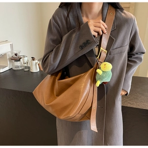 Detail of a brown hobo shoulder bag with a cute green turtle plush pendant on the strap