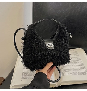 Close-up of black curly plush handbag with silver twist lock and leather handle on book