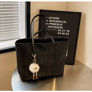 Detail view of black textured tote bag with fluffy white pompom charm and logo patch