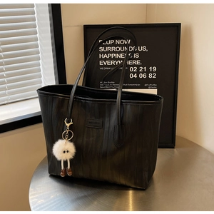Detail of black tote bag with vertical wave texture and cute plush charm on a table