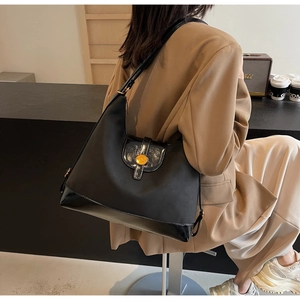 Detail of black large capacity shoulder bag featuring glossy patent leather and gold buckle