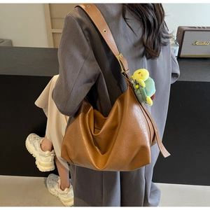 Detailed view of coffee brown large tote bag with cute green turtle charm on shoulder