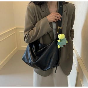 Detail of black faux leather tote bag with wide strap and green turtle plush charm