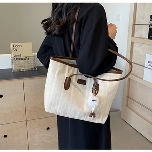 Detail of off-white wave textured tote bag with brown trim and plush charm on a shoulder