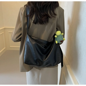 Large black faux leather tote bag worn by model, featuring a green plush turtle charm