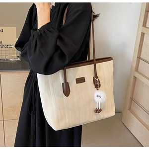 Detail of large beige tote bag with brown straps and white plush pendant on a model