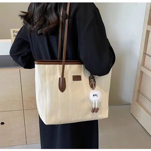 Detailed macro view of cream textured fabric tote bag with brown leather handles and charm