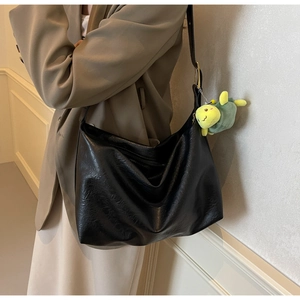 Detail of black faux leather tote bag with vintage texture and green plush turtle charm