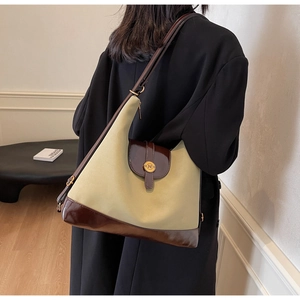 Detail of canvas tote bag with leather flap and golden N-letter buckle on model