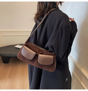 Detail of dark brown suede shoulder bag featuring symmetrical front flap pockets