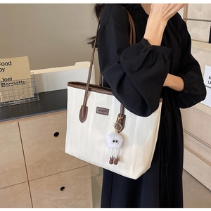 Detail of cream tote bag with brown trim and plush charm in a cozy home setting
