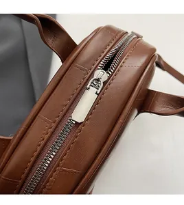 Detailed close-up of smooth silver metal zipper on brown crocodile pattern leather bag