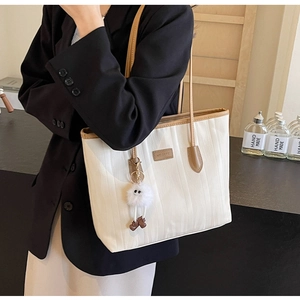 Detail of white pleated tote bag featuring brown leather straps and plush charm