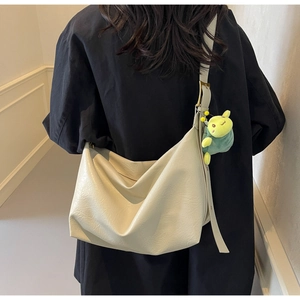 Detail of a creamy white oversized hobo bag featuring soft pleats and a green plush charm