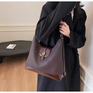 Detail of a deep brown canvas tote bag featuring an N-engraved metallic buckle