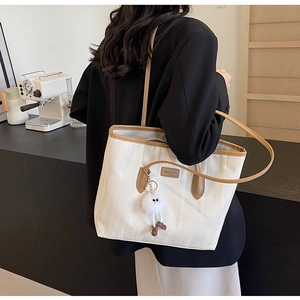 Detail of canvas tote bag with brown leather trim and cute plush ball charm
