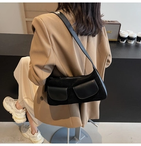 Side view of a large black matte suede shoulder bag worn by a model in a cafe