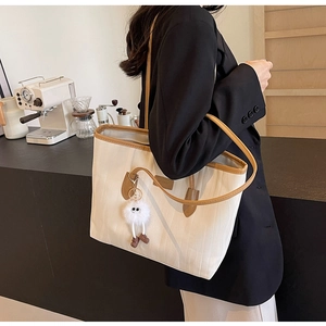 Detail of a large cream tote bag with brown leather trim and a plush monster charm