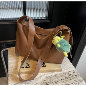 Detail of brown leather tote bag with a cute green plush turtle charm on the shoulder strap