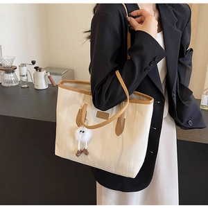 Close-up of cream tote bag featuring brown leather trim and a white plush toy charm