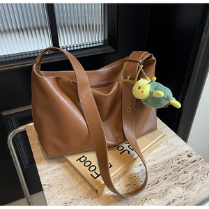 Close-up of brown tote bag featuring a gold buckle and a lime green plush pendant charm