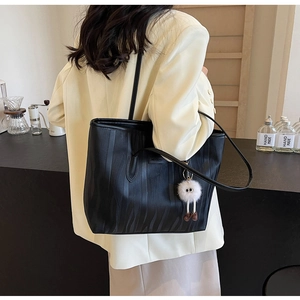 Detail of black tote bag with wave texture and cute plush charm on a beige blazer