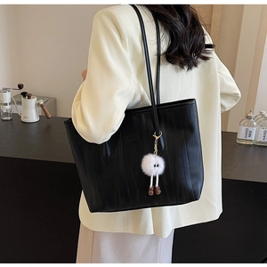 Detail of black faux leather tote bag with vertical stripes and a cute plush monster charm