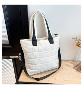 Close-up of white quilted nylon tote bag with black straps and zip closure on marble