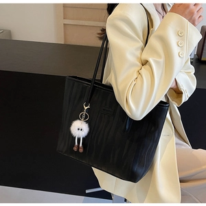 Detail of black tote bag with vertical wave texture and cute plush monster charm