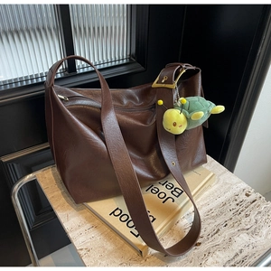 Close-up of brown faux leather tote bag with gold buckle and green turtle plush charm