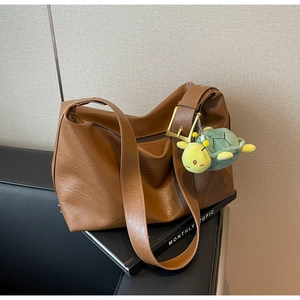 Detail of a brown PU leather hobo bag with a gold buckle and green turtle plush charm