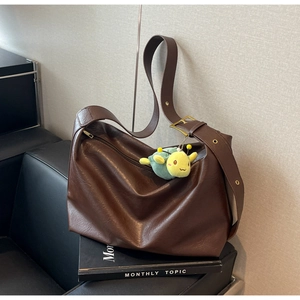 Detail of dark brown faux leather hobo bag with wide strap and caterpillar charm