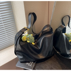 Detail of black large tote bag with wide strap, gold buckle and green turtle charm