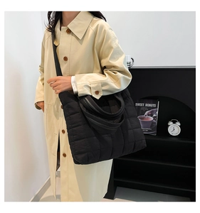 Close-up of a black quilted nylon tote bag with wide shoulder strap and soft padded handles