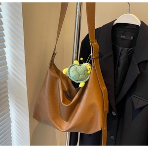 Close-up of brown oversized tote bag with wide strap and cute green turtle charm