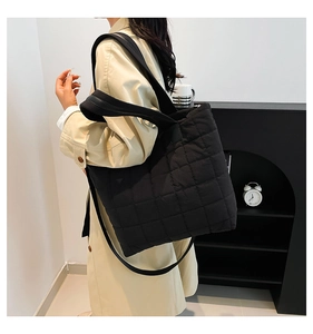 Detail of black quilted nylon tote bag with wide strap on shoulder of model in trench coat