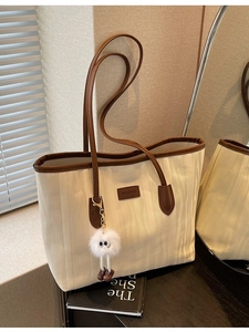 Chic cream canvas tote bag with brown leather trim and plush monster charm on black desk