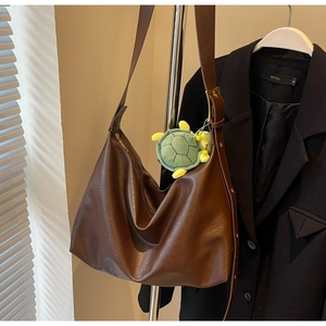 Detail of a brown leather Hobo bag with a green plush turtle pendant hanging on the strap